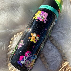 May include: Black Owala water bottle with a galaxy-themed design, featuring cartoon characters like Care Bears, Garfield, and My Little Pony. The bottle has a black lid with a green and yellow handle.