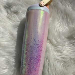 May include: A pink and white iridescent glitter tumbler with a light blue lid and a beige handle.
