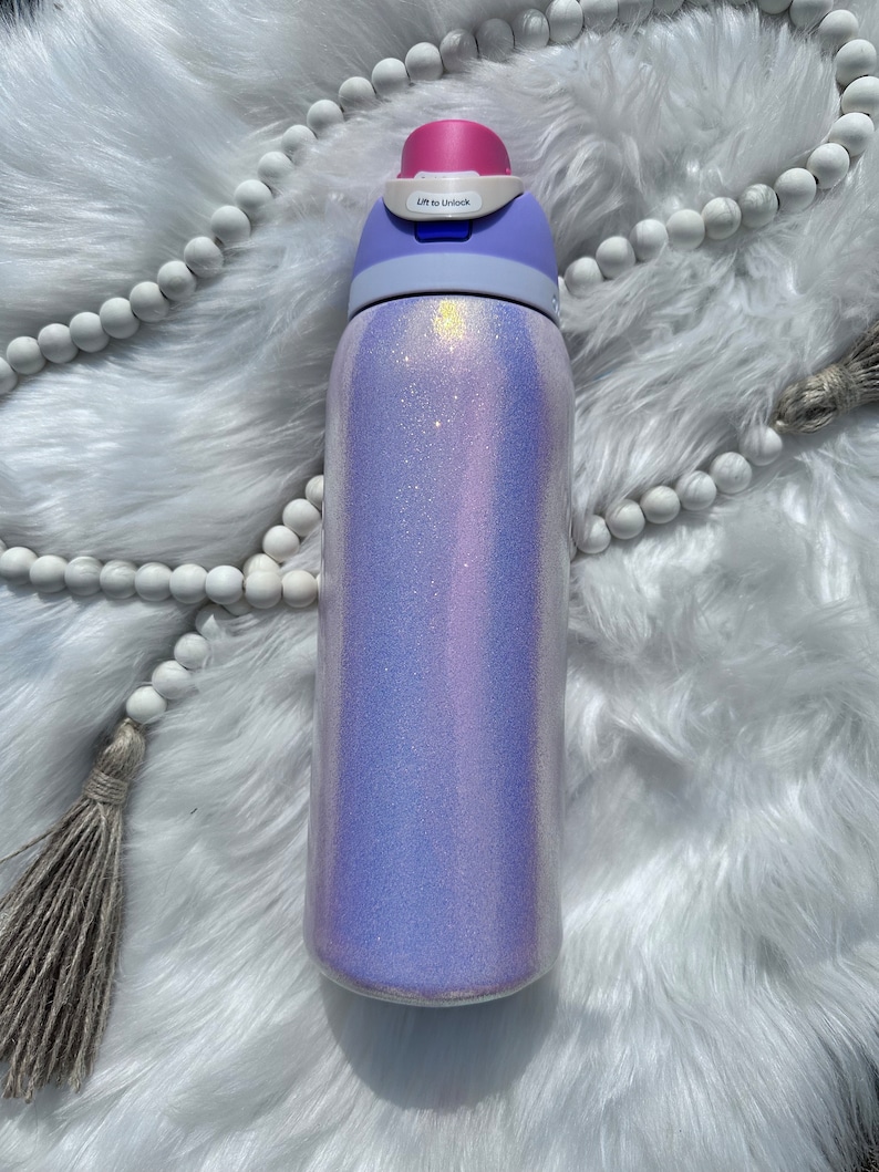 Op de afbeelding: Een paarse en witte glitterwaterfles met een blauw en roze deksel. Het deksel heeft de tekst "Lift to Unlock" erop.