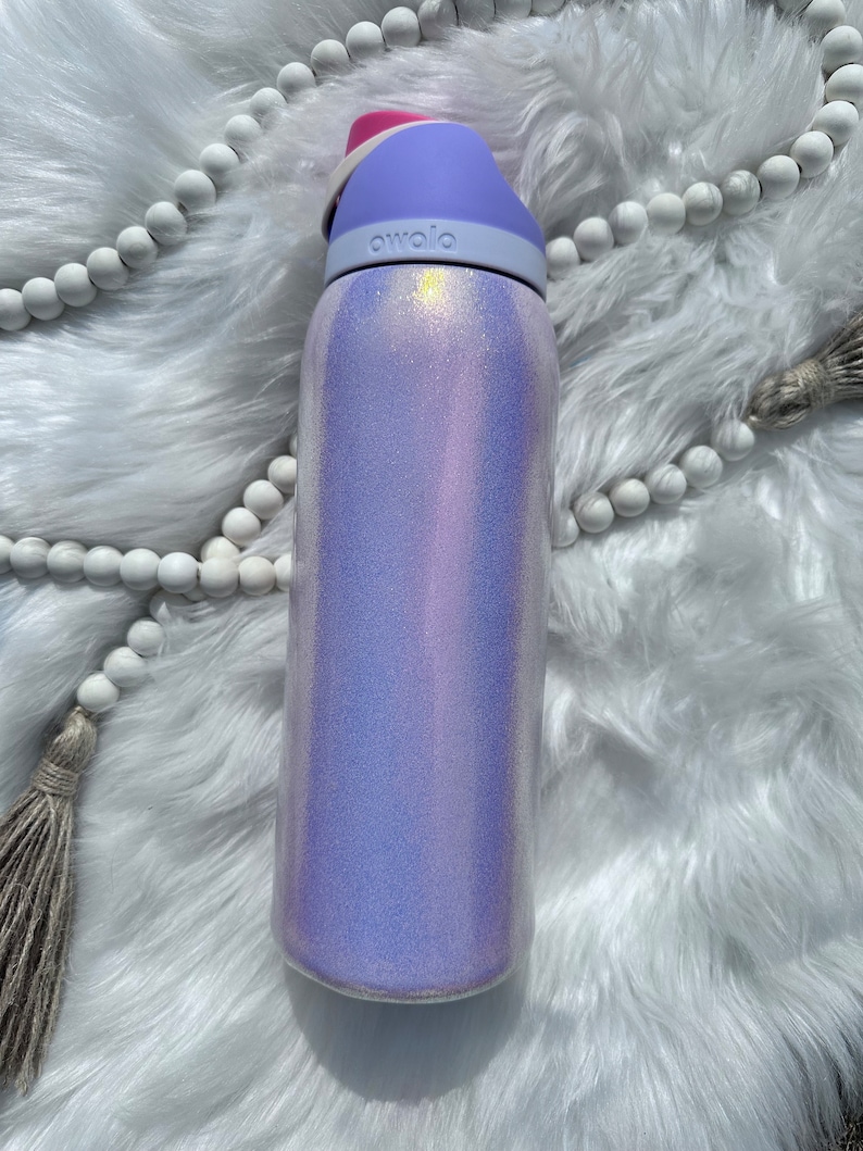 Op de afbeelding: Een herbruikbare waterfles in paars en wit met een roze deksel en het woord "avolo" gedrukt op de zijkant.