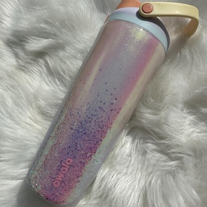 May include: A pink and white iridescent water bottle with a glitter finish and a yellow handle. The bottle has the word "owala" printed on the side.