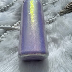 Op de afbeelding: Een paarse en witte glitterbeker met een lichtgele, iriserende glans. De beker heeft een schroefdop en een brede opening.