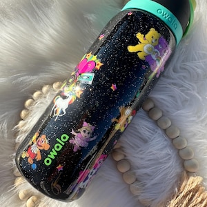 May include: Black Owala water bottle with a variety of cartoon characters and a starry night design. The bottle features a black lid, a teal handle, and the Owala logo in green. The bottle is decorated with Care Bears, unicorns, and other colorful graphics.