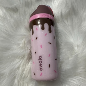 Op de afbeelding: Roze en bruine geïsoleerde waterfles met een chocolade- en sprinkelingontwerp. De fles heeft het woord "owala" erop gedrukt.