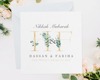 May include: A white wedding invitation with gold lettering that reads "Nikkah Mubarak" and features the letters "H" and "F" decorated with green eucalyptus leaves. The text below reads "Hassan & Fariha The Twenty-Third of May".