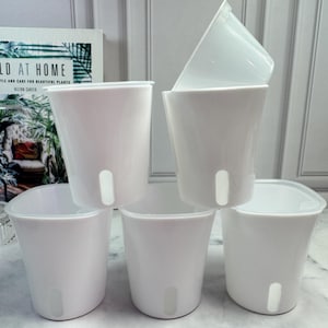 May include: A stack of six white plastic plant pots. Each pot has a rounded shape with a drainage hole and a slightly flared rim. One pot is upside down on top of the stack.