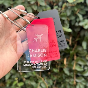 May include: Clear acrylic luggage tag with a white airplane design and the text "Charlie Jamison" and contact information. The tag is attached to a silver metal cable.