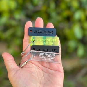 May include: Three keychains with black and clear acrylic tags. The top tag says "JACQUELINE" in black text. The middle tag says "CHRISTOPHER" in black text and "123-435-1234" in white text. The bottom tag says "JACQUELINE" in black text, "CHRISTOPHER" in black text, "123 EVYLLITTLEDESIGN" in black text, "MISSION, CA 92699" in black text, and "123-456-9876" in black text.