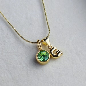 May include: A gold chain necklace with two charms: a green gemstone and a gold letter 'G'.