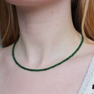 May include: A delicate green jade necklace with small round beads. The necklace is worn by a person with a white crocheted top.