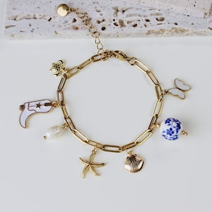 May include: Gold charm bracelet featuring a range of charms, including a cowboy boot, a seashell, a starfish, a butterfly, a pearl, and a blue and white porcelain bead.