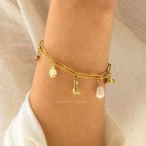 May include: A gold charm bracelet with a variety of charms, including a four-leaf clover, a boot, and a pearl. The bracelet is on a person's wrist.