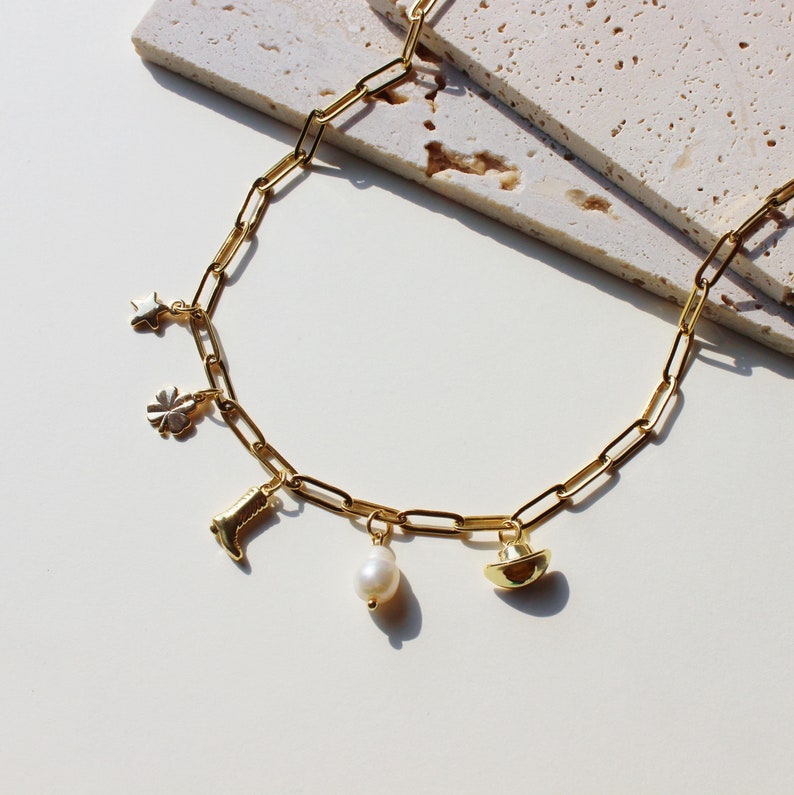 Puede incluir: Un collar de cadena dorada con dijes que incluyen una estrella, un tr&eacute;bol de cuatro hojas, una bota, una perla y un sombrero.
