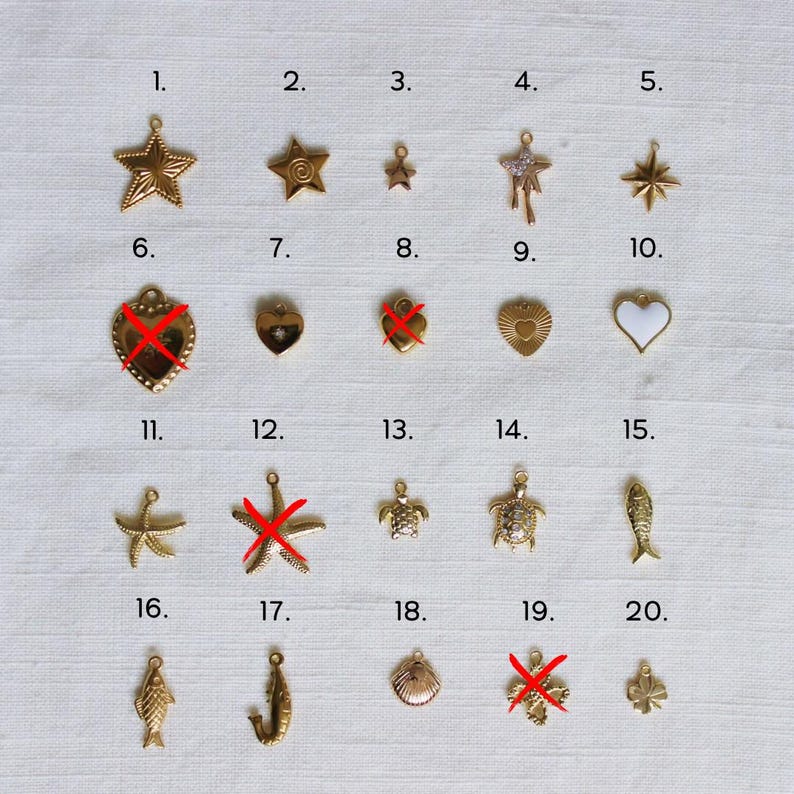 May include: A collection of gold-colored charms in various shapes, including stars, hearts, a turtle, a fish, and a seashell. Some charms have a textured surface, while others are smooth. The charms are arranged on a light-colored surface.