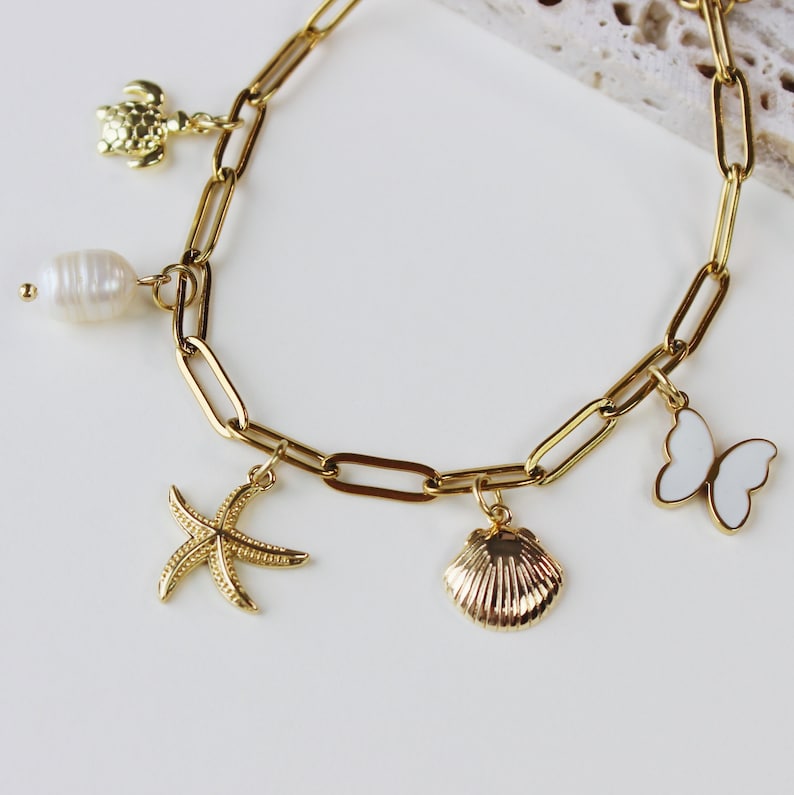 Peut inclure: Bracelet en cha&icirc;ne dor&eacute;e avec des breloques, dont une perle, une &eacute;toile de mer, un coquillage et un papillon.