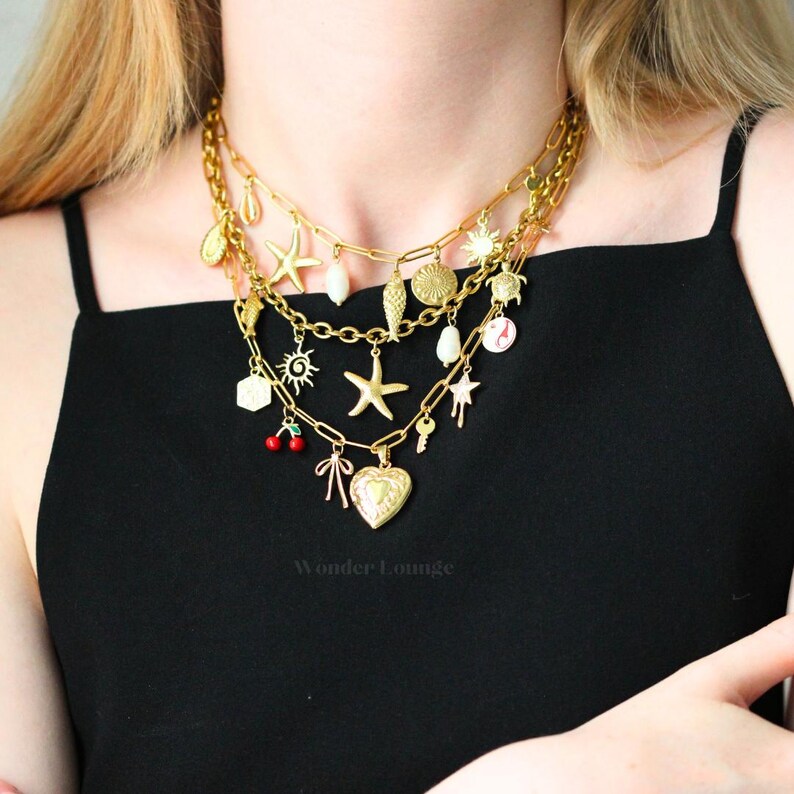 May include: Gold-toned layered necklaces with various charms, including starfish, shells, suns, and a heart-shaped locket. The necklaces are worn against a black top, creating a contrast that highlights the jewelry's details.