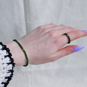 May include: A green jade bracelet and ring set with gold accents. The bracelet and ring are made of small, round beads.