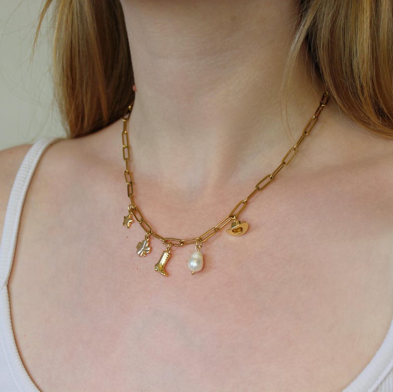 Puede incluir: Un collar de cadena dorada con una variedad de dijes, que incluyen una bota, un tr&eacute;bol de cuatro hojas, una estrella y una perla. El collar lo lleva una persona con el pelo largo y rubio.