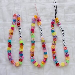 May include: Three colorful beaded phone charms with the names "Jess", "Lucy", and "Isabelle" spelled out in white beads. Each charm features a variety of fruit and flower beads in pink, yellow, green, blue, and purple.
