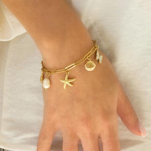 Peut inclure: Bracelet en or avec des breloques en forme d'&eacute;toile de mer, de coquillage, de perle et de papillon.