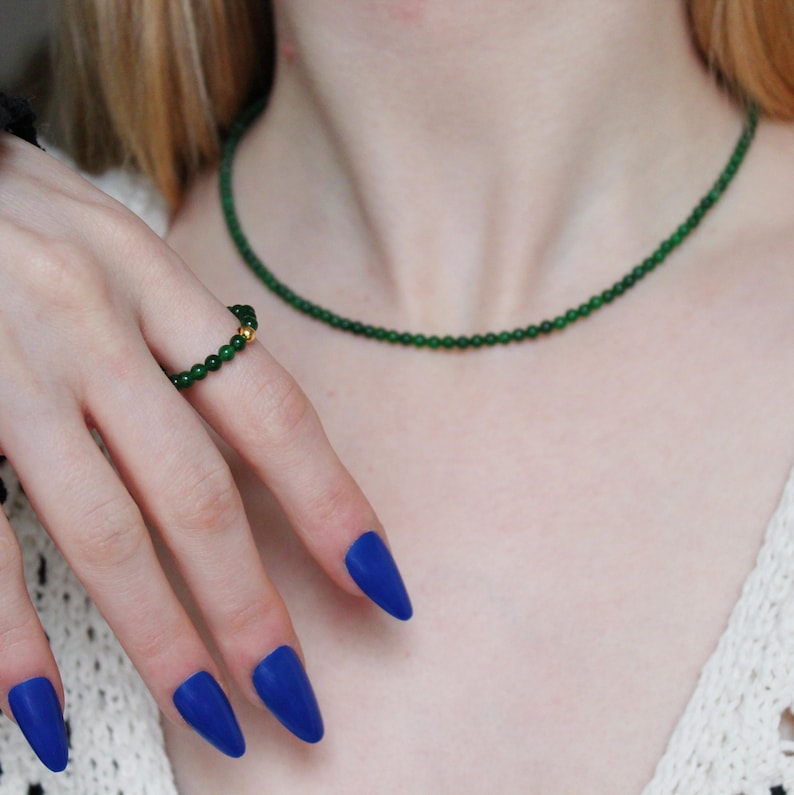 May include: A green jade necklace and ring set. The necklace is made of small, round beads and the ring is a simple band with a small green jade stone.