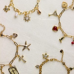 May include: Gold-toned charm bracelets with various pendants, including a turtle, sun, seashell, starfish, cross, and heart. The charms are detailed with crystals and pearls. The bracelets are displayed on a white surface.