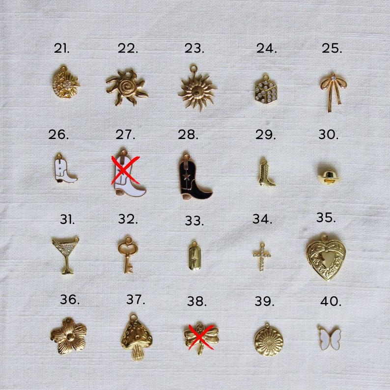 May include: A collection of gold-colored charms, including a sunflower, spider, sun, bow, cowboy boots, martini glass, key, cross, heart locket, flower, mushroom, and butterfly. Each charm is numbered from 21 to 40.