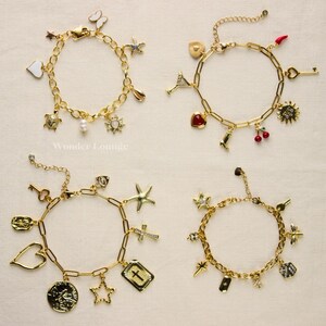 May include: Four gold-colored charm bracelets with various pendants, including stars, hearts, crosses, and a turtle. The bracelets have a chain link design and are displayed on a light-colored surface. The bracelets are from Wonder Lounge.