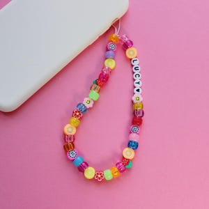 May include: A colorful phone charm with fruit and flower beads, a smiley face bead, and the name "LUCY" spelled out in white beads.
