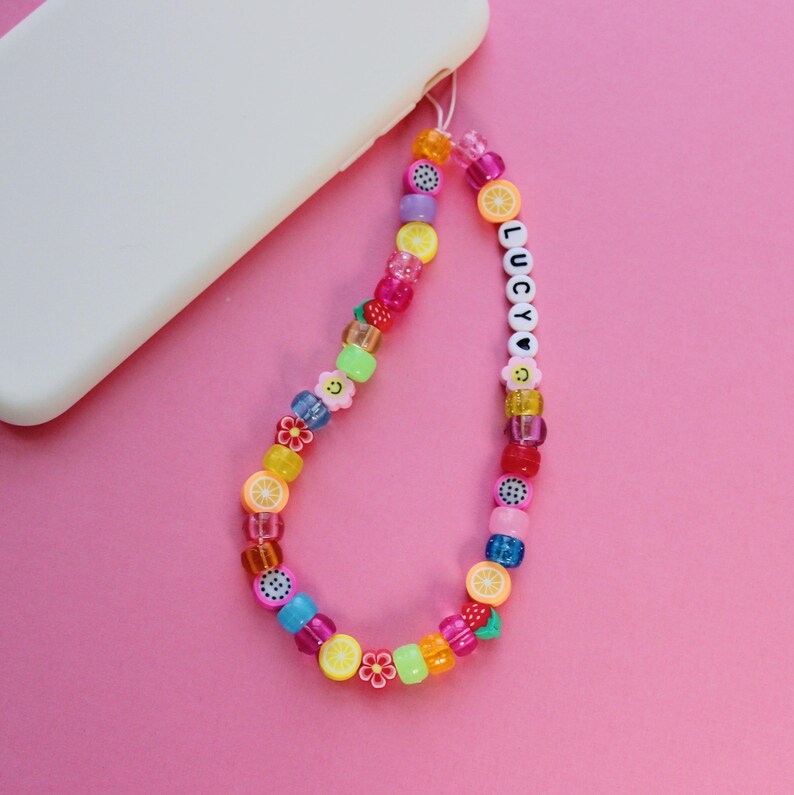 May include: A colorful phone charm with fruit and flower beads, a smiley face bead, and the name "LUCY" spelled out in white beads.