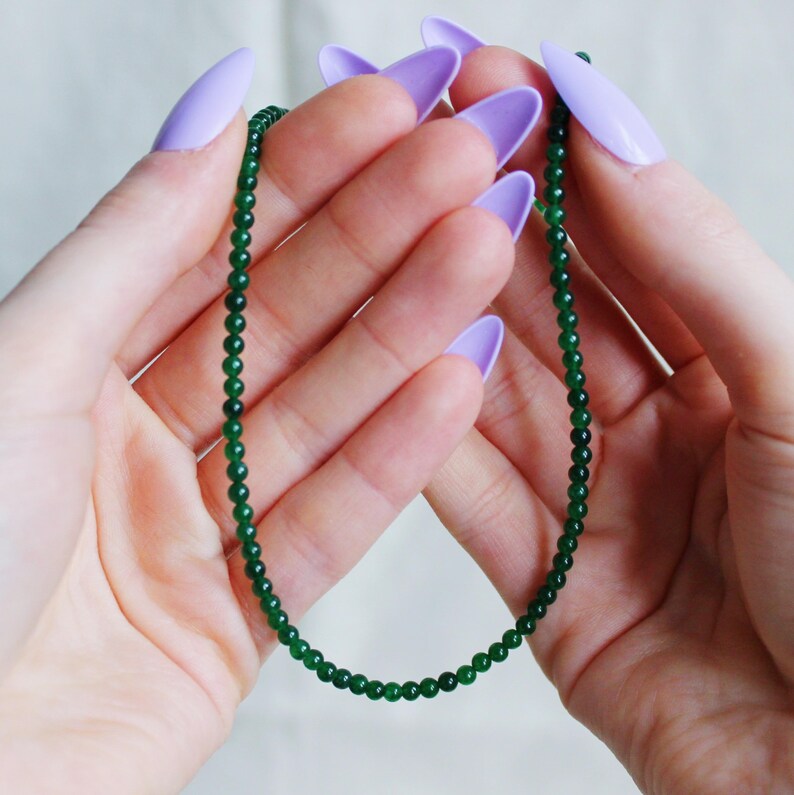 May include: A green jade bead necklace with small, round beads. The necklace is held in the hands of a person.