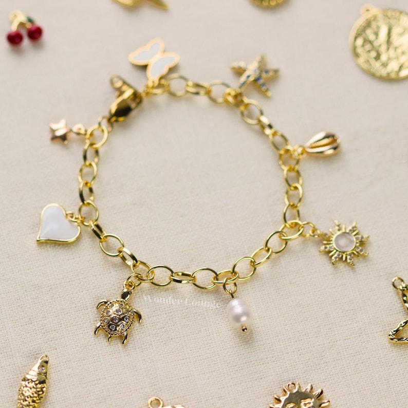 May include: Gold-toned charm bracelet featuring various pendants, including a white heart, a butterfly, a star, a sunburst, a turtle, and a pearl. The bracelet has an oval link chain and a lobster clasp.