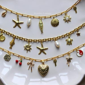 May include: Gold-toned charm necklaces with various pendants, including starfish, shells, pearls, and a heart-shaped locket. The necklaces are arranged on a white surface. The text "Wonder Lounge" is visible.