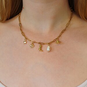 Puede incluir: Un collar de cadena dorada con varios colgantes, incluyendo una estrella, un tr&eacute;bol de cuatro hojas, una bota, una perla y un peque&ntilde;o sombrero.