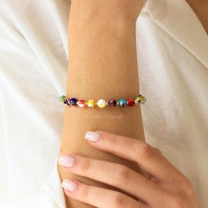 May include: A colorful beaded bracelet with a gold chain and various colored glass beads with a white and gold design. The beads are in a rainbow pattern.