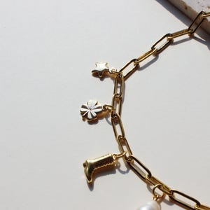 Puede incluir: Un brazalete de cadena dorada con dijes, incluyendo una estrella, un tr&eacute;bol de cuatro hojas, una bota y una perla.