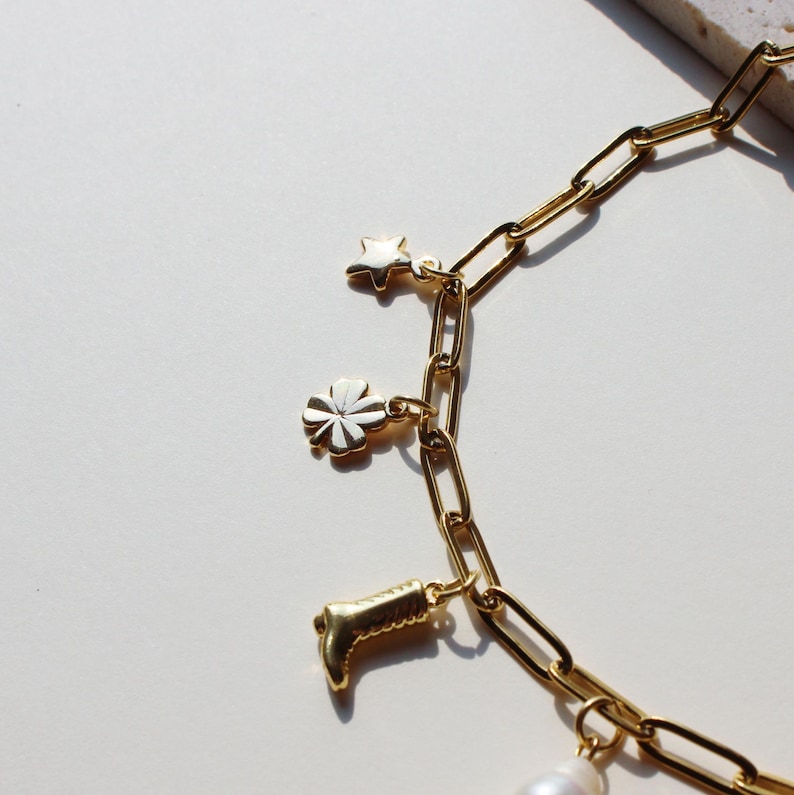 Puede incluir: Un brazalete de cadena dorada con dijes, incluyendo una estrella, un tr&eacute;bol de cuatro hojas, una bota y una perla.
