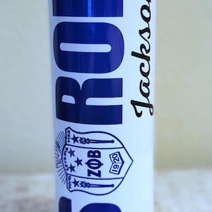 May include: A white tumbler with blue text that reads "SR BOR" vertically and "Jackson" in a cursive font. A blue emblem with the letters "ZOB" and the year "1920" is also visible.