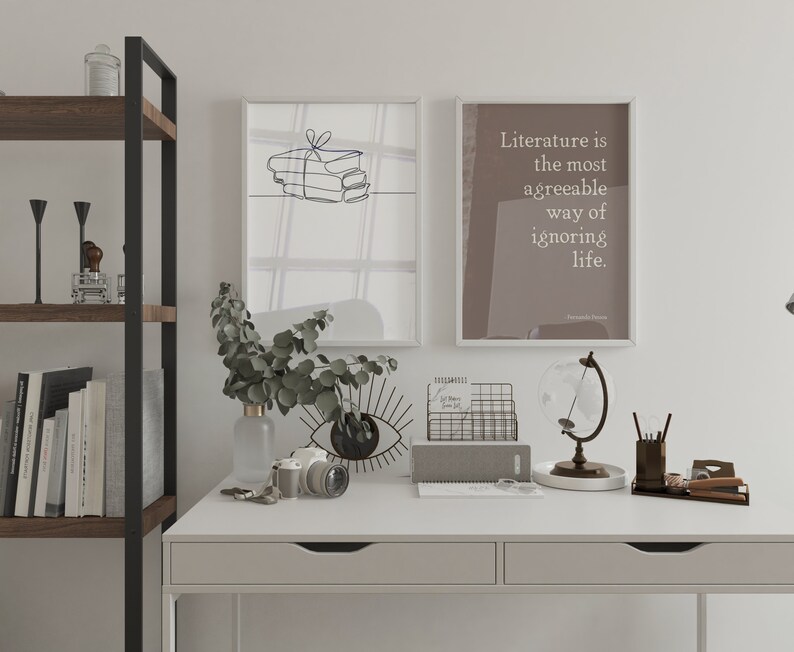 Puede incluir: Un escritorio blanco con dos cajones, una estanter&iacute;a de metal negro y dos impresiones enmarcadas. La impresi&oacute;n de la izquierda presenta un dibujo lineal de una pila de libros con una cinta. La impresi&oacute;n de la derecha tiene un fondo marr&oacute;n con texto blanco que dice "La literatura es la forma m&aacute;s agradable de ignorar la vida." El escritorio tiene una variedad de art&iacute;culos sobre &eacute;l, incluyendo un jarr&oacute;n con hojas verdes, una c&aacute;mara, un globo terr&aacute;queo, un portacartas de alambre y una libreta gris.