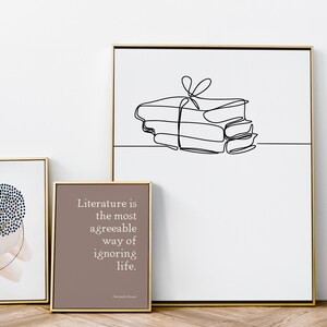 Puede incluir: Tres impresiones enmarcadas con marcos dorados. La impresi&oacute;n de la izquierda presenta un dise&ntilde;o abstracto azul y blanco sobre un fondo de acuarela rosa. La impresi&oacute;n del centro presenta un fondo marr&oacute;n con texto blanco que dice "La literatura es la forma m&aacute;s agradable de ignorar la vida." La impresi&oacute;n de la derecha presenta un dibujo de l&iacute;nea negra de una pila de libros atados con una cinta.