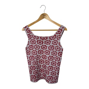 Pode incluir: Um top sem mangas com decote quadrado, apresentando um padrão floral repetido em vermelho sobre um fundo cinza claro. O top está pendurado em um cabide de madeira contra um fundo branco.