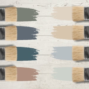 May include: Eight paintbrushes with natural bristles and silver ferrules, each displaying a different color swatch. The colors include shades of gray, blue, and beige, arranged on a white wooden surface.