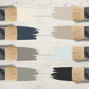 May include: An overhead shot of eight paintbrushes, each with a different color swatch. The colors include cream, navy blue, taupe, light blue, gray, and black. The paintbrushes are arranged on a white wooden surface.