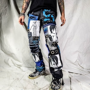 Model showing the black pants with anime prints, colorful patchwork in multiple blue shades, ripped patches, zipper, eyelets, studs and abstract painting with a blue snake on the front.