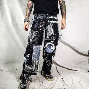 May include: Black and white patched denim trousers with a skull and crossbones design, a smiley face, and other graphic details. The trousers have a distressed look and are worn with a black t-shirt.