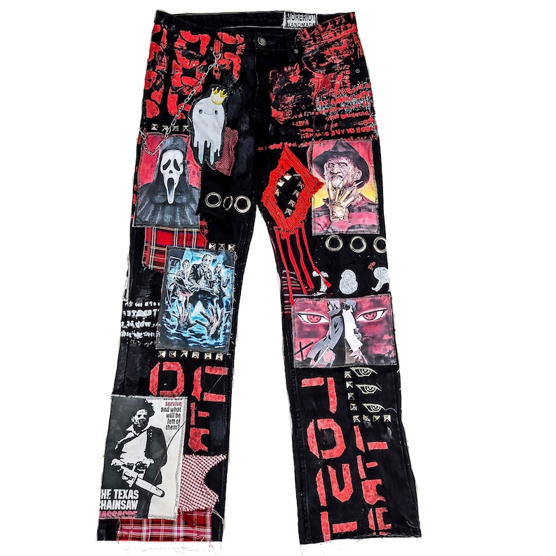 Flad laid jeans showing a custom made black pair with prints containing various horror movies, red and black patchwork, abstract painting, studs, red laces hanging down, chain and eyelets.