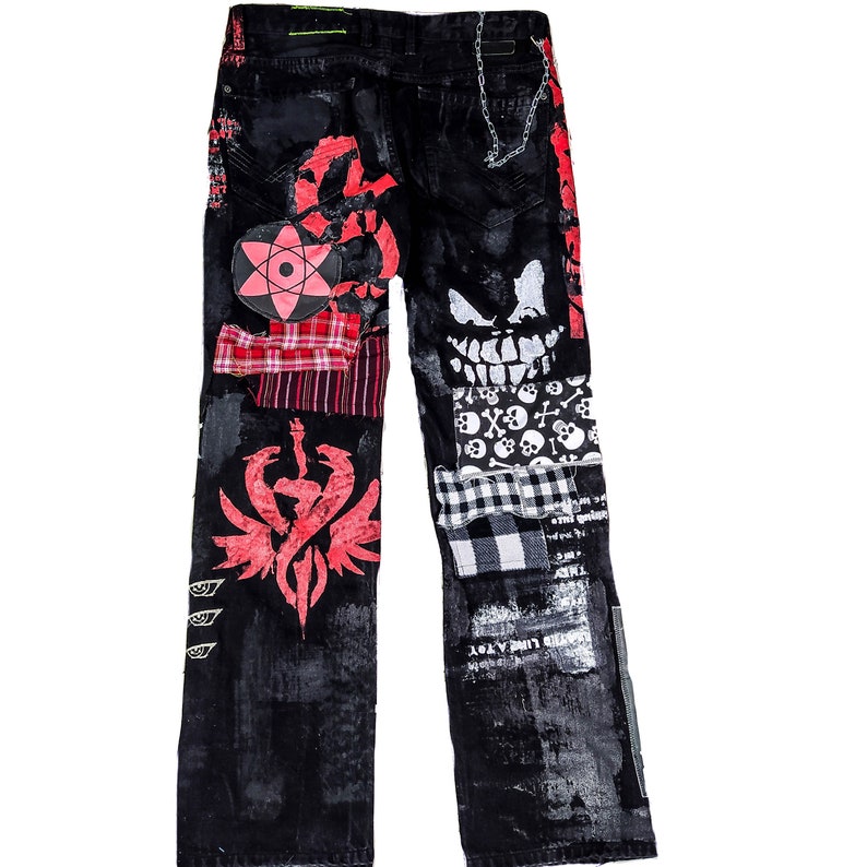 Flad laid jeans showing a custom made black pair with prints containing various horror movies, red and black patchwork, abstract painting, studs, red laces hanging down, chain and eyelets.