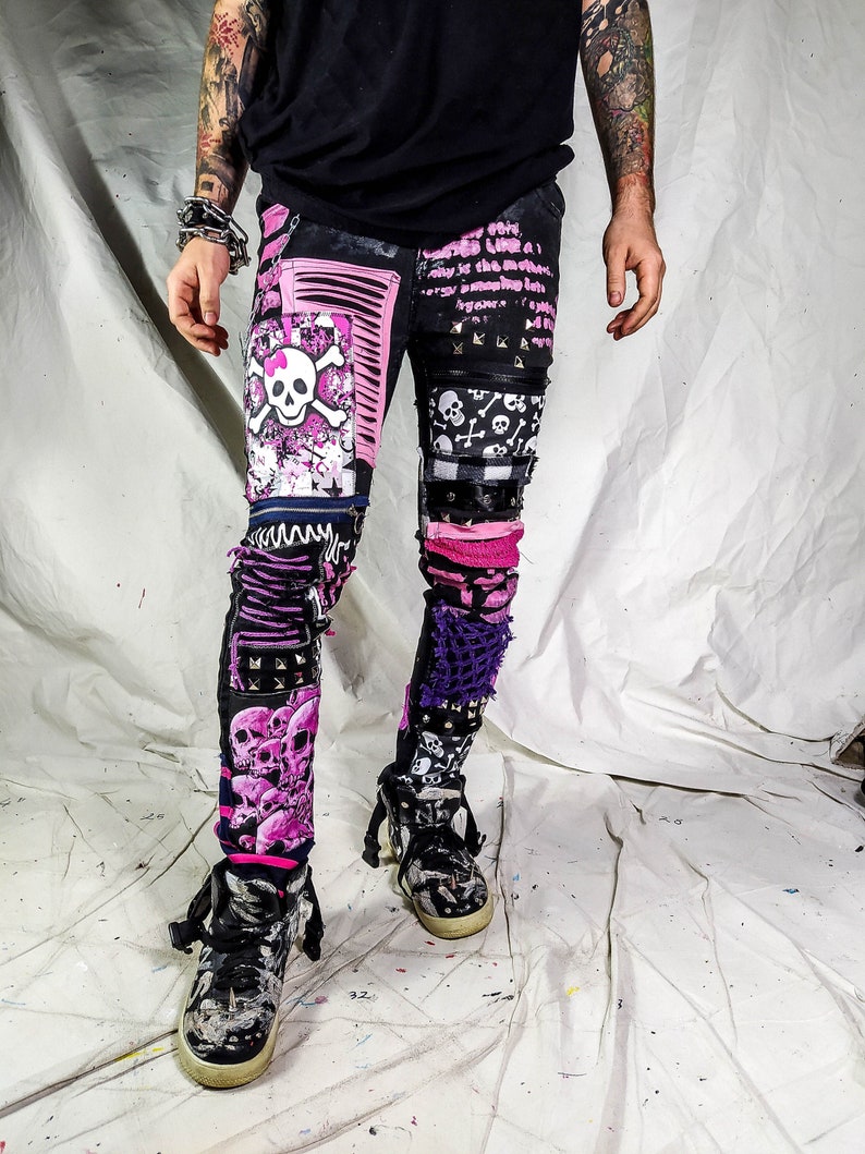 Model showing a pair of pink and black add ons on black pants, such as pink and white skulls, zippers, studs, purple laces and chain, abstract paint and patchwork.