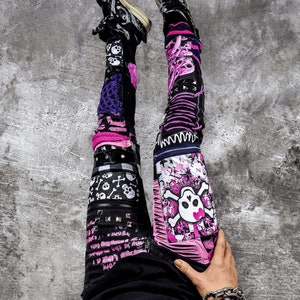 Model showing a pair of pink and black add ons on black pants, such as pink and white skulls, zippers, studs, purple laces and chain, abstract paint and patchwork.