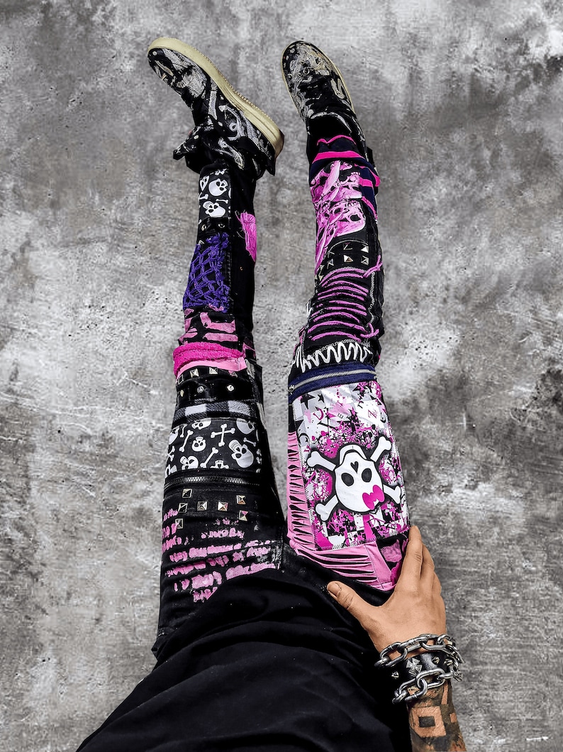 Model showing a pair of pink and black add ons on black pants, such as pink and white skulls, zippers, studs, purple laces and chain, abstract paint and patchwork.